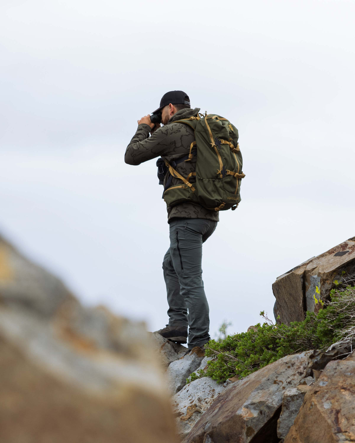 Hunter standing in a distance using his binocular, wearing Ridgepoint Fleece Hoodie in Ash Tonal Brown