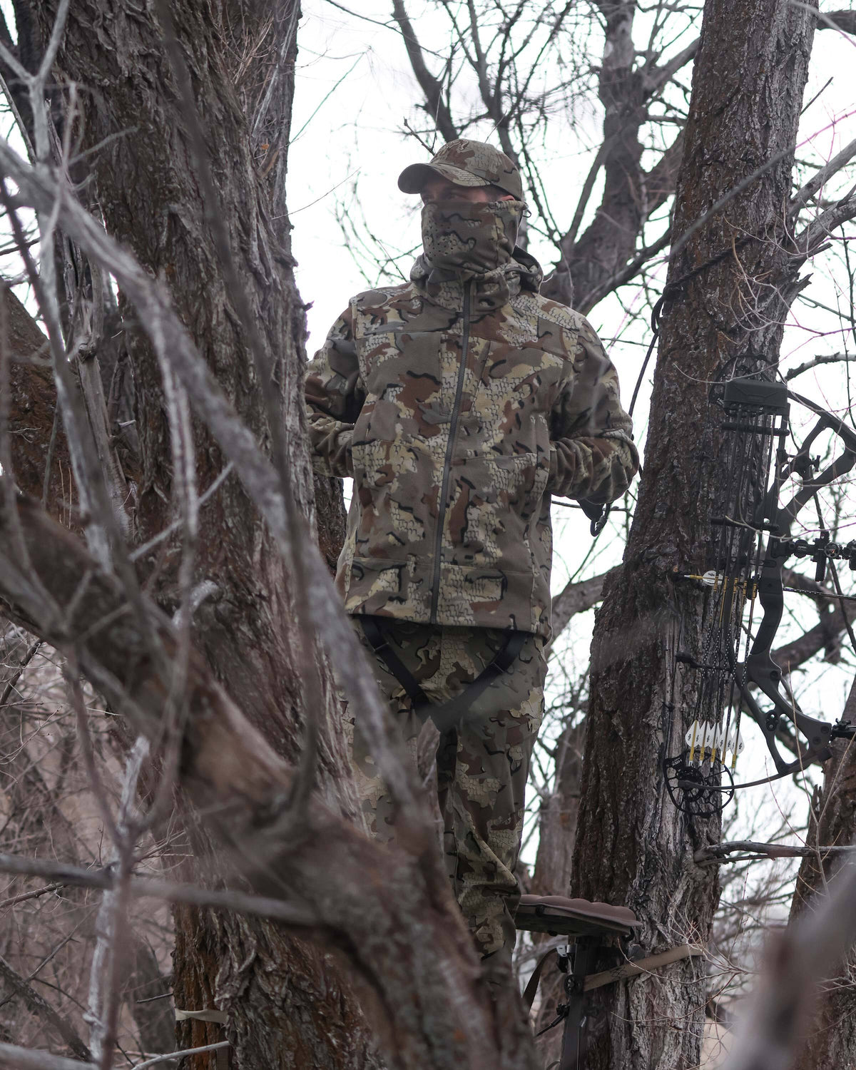 Bowhunter standing camouflaged in a tree stand with hands in his pocket, wearing Proximity LT Hooded Jacket in Valo Camouflage