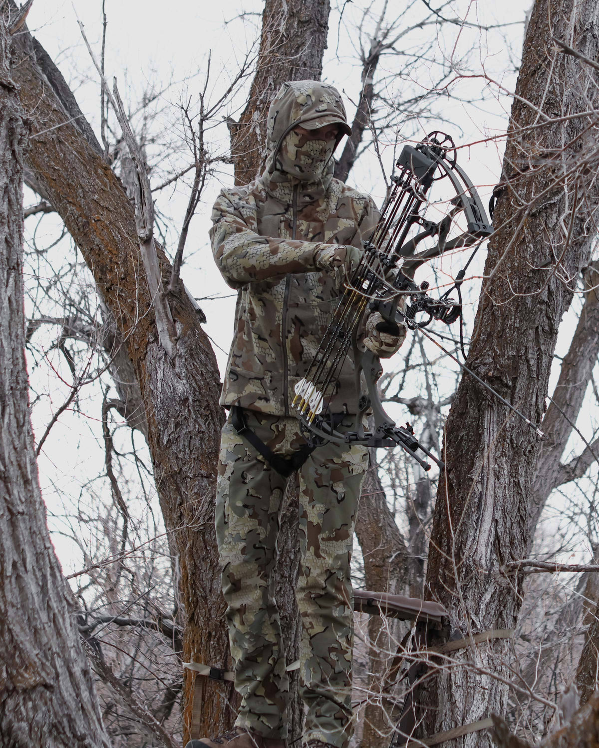 Bowhunter holding bow and arrow. standing in the tree stand, wearing Proximity LT Hooded Jacket in Valo Camouflage