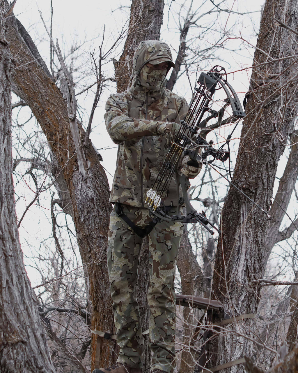 Bowhunter holding bow and arrow. standing in the tree stand, wearing Proximity LT Hooded Jacket in Valo Camouflage