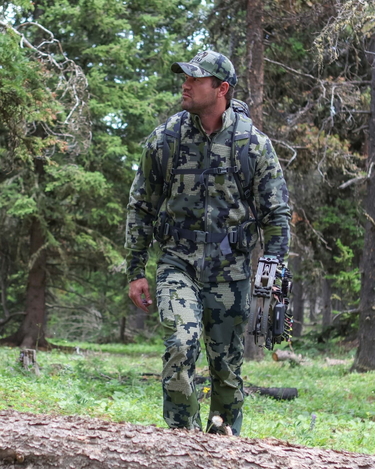 Hunter hiking through the forest wearing Border Fleece Full Zip Jacket in Verde Camouflage