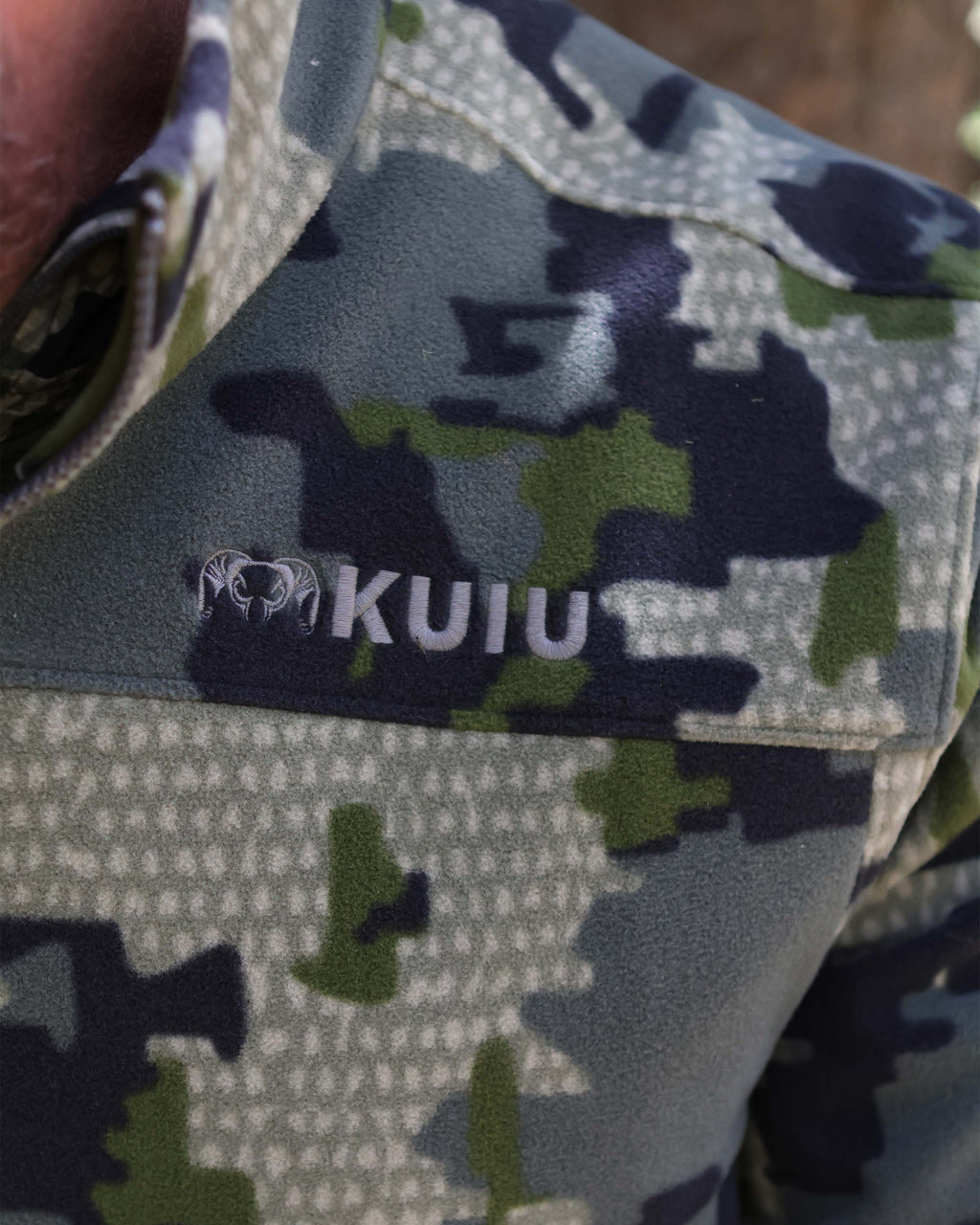 Close-up of embroidered KUIU logo on the front left chest of Border Fleece Full Zip Jacket in Verde Camouflage