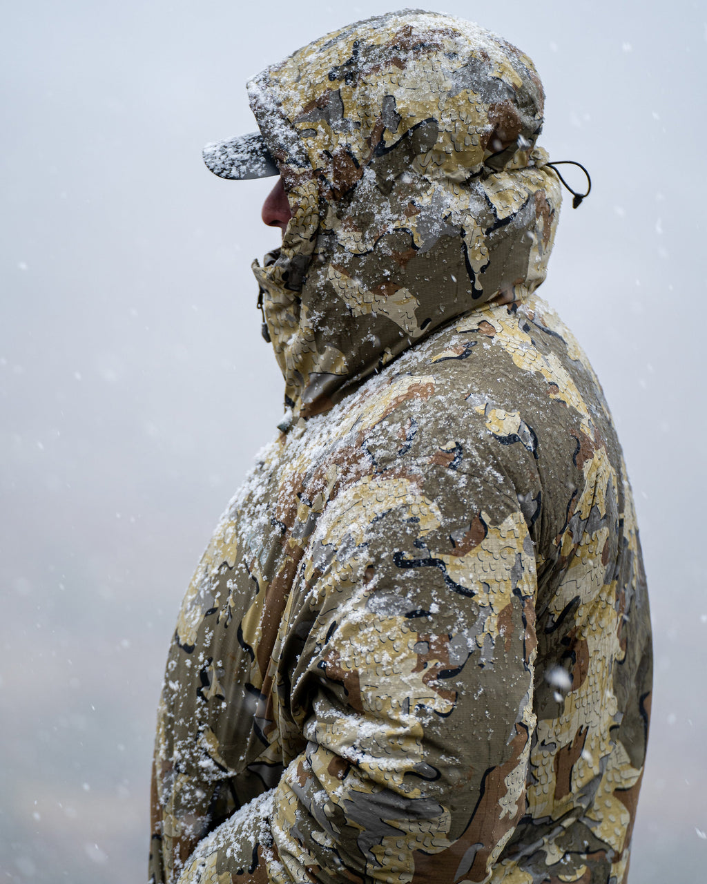 Side of hunter standing in snow storm wearing Super Down Burner Parka in Valo Camouflage