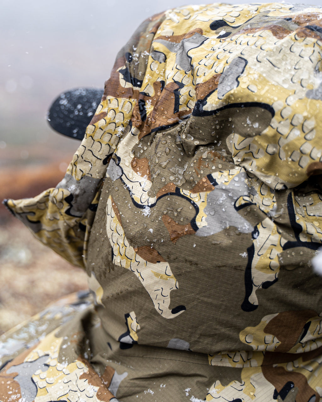 Back detail of hood on Super Down Burner Parka in Valo Camouflage collecting snow and beading water
