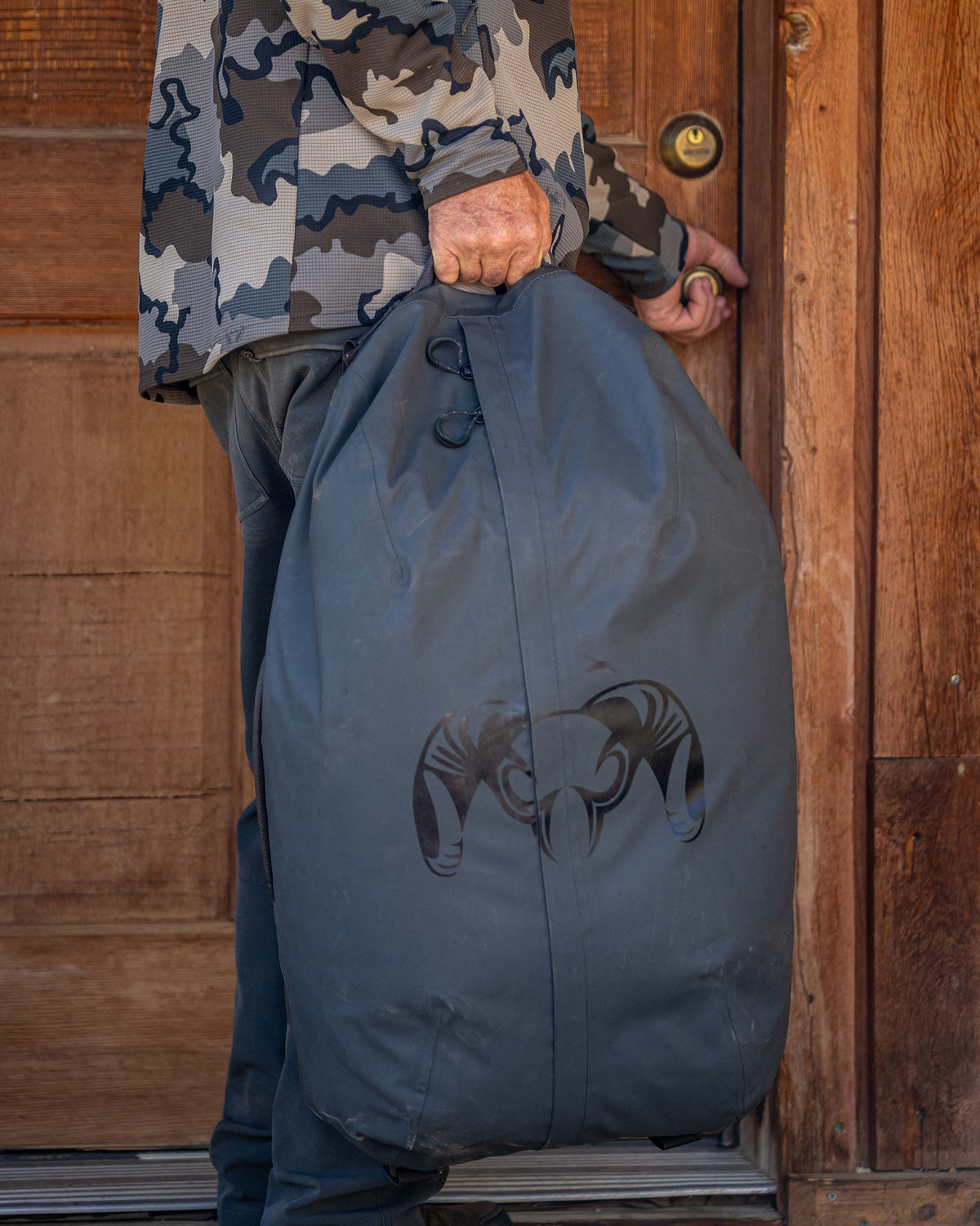 Hunter grasps front door doorknob while holding Taku BLSTX 4200 Duffel in Gunmetal Grey