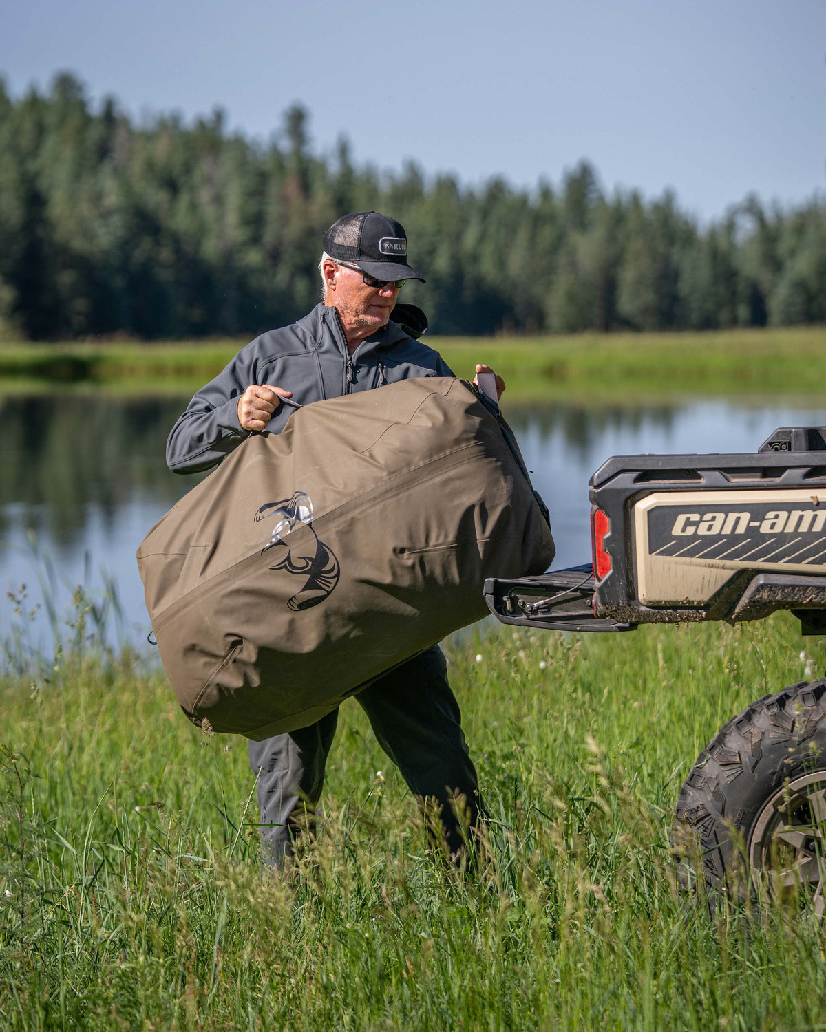 Hunter lifts and places a Taku BLSTX 10000 Duffel in Bourbon Brown into the cargo bed of a UTV