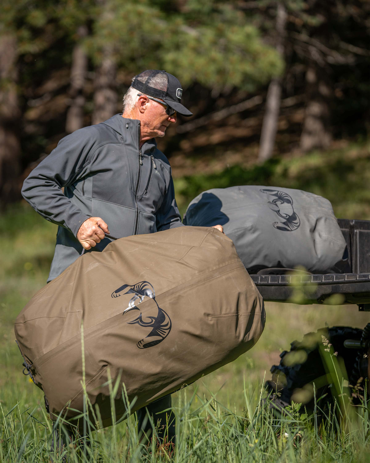 Hunter loads Taku BLSTX 10000 Duffels in Bourbon Brown and Gunmetal Grey into the back of a UTV
