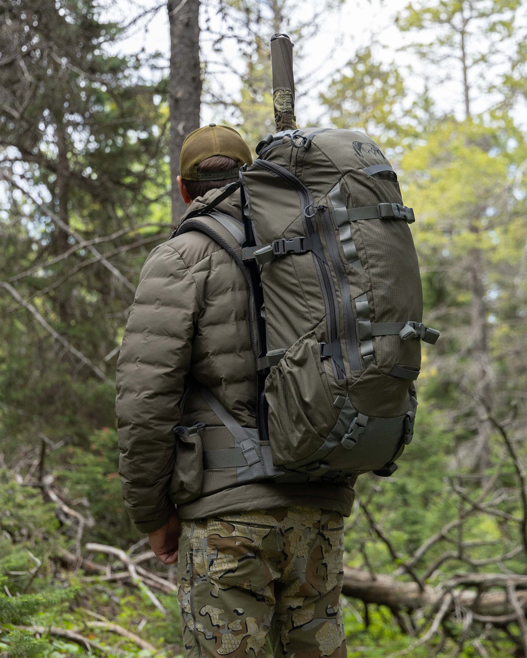 Back view of hunter carrying ICON 6 3500 Pack in Ash Brown in a forest setting.