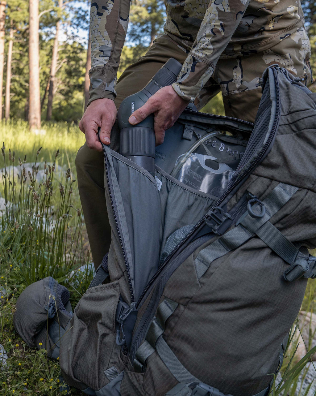 Hunter packing a spotting scope into the back pocket of the ICON 6 3500 Pack in Ash Brown.