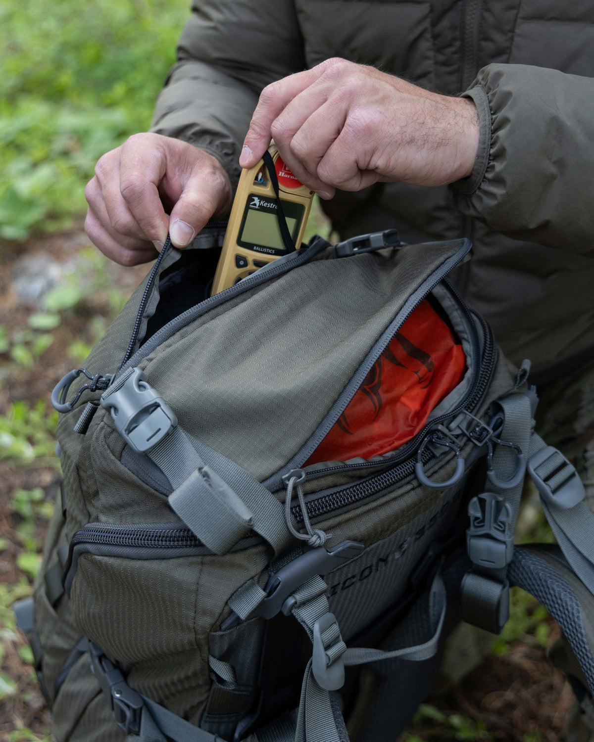 Hunter opening top back of ICON 6 Pack in Ash Brown, stowing a Kestral weather meter inside.