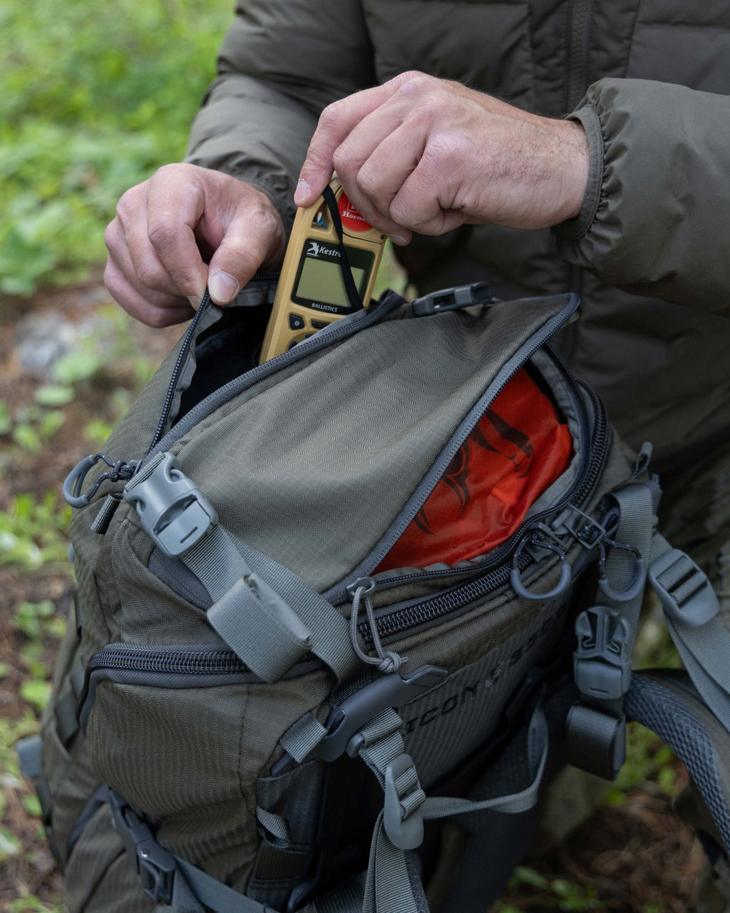 Hunter opening top back of ICON 6 Pack in Ash Brown, stowing a Kestral weather meter inside.