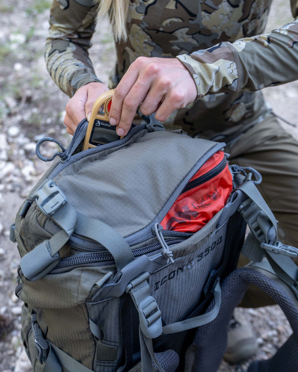 Hunter stowing a pocket weather meter in the ICON 6 3500 Pack in Ash Brown.