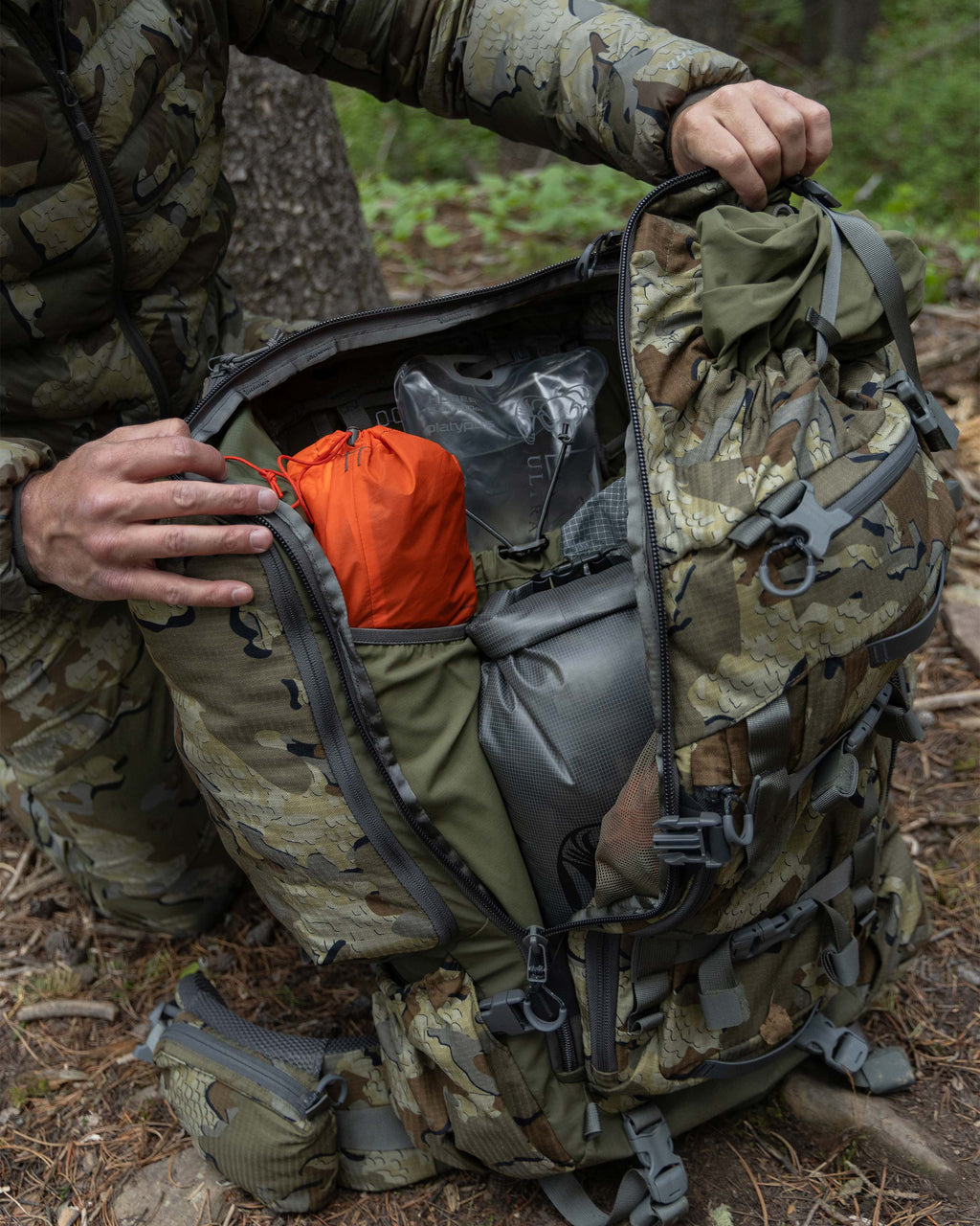 Hunter in a forest setting showcasing items inside the main compartment of ICON 8200 Pack in Valo Camouflage.