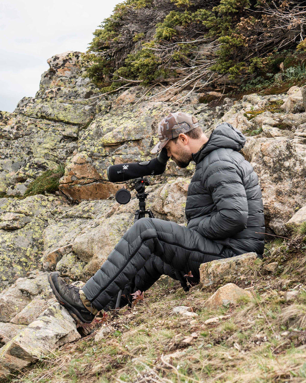 Hunting Glassing in Rocky Terrain Through Spotting Scope with Super Down LT Hooded Jacket and Pants in Gunmetal Grey