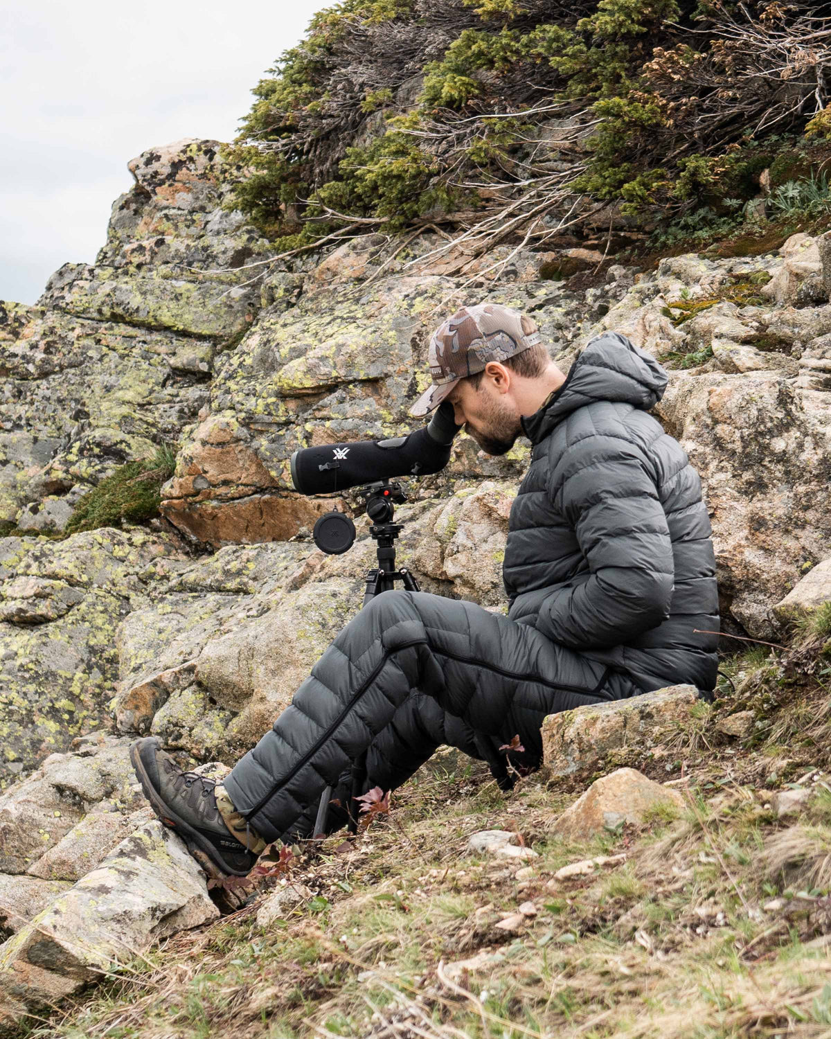 Hunting Glassing in Rocky Terrain Through Spotting Scope with Super Down LT Hooded Jacket and Pants in Gunmetal Grey