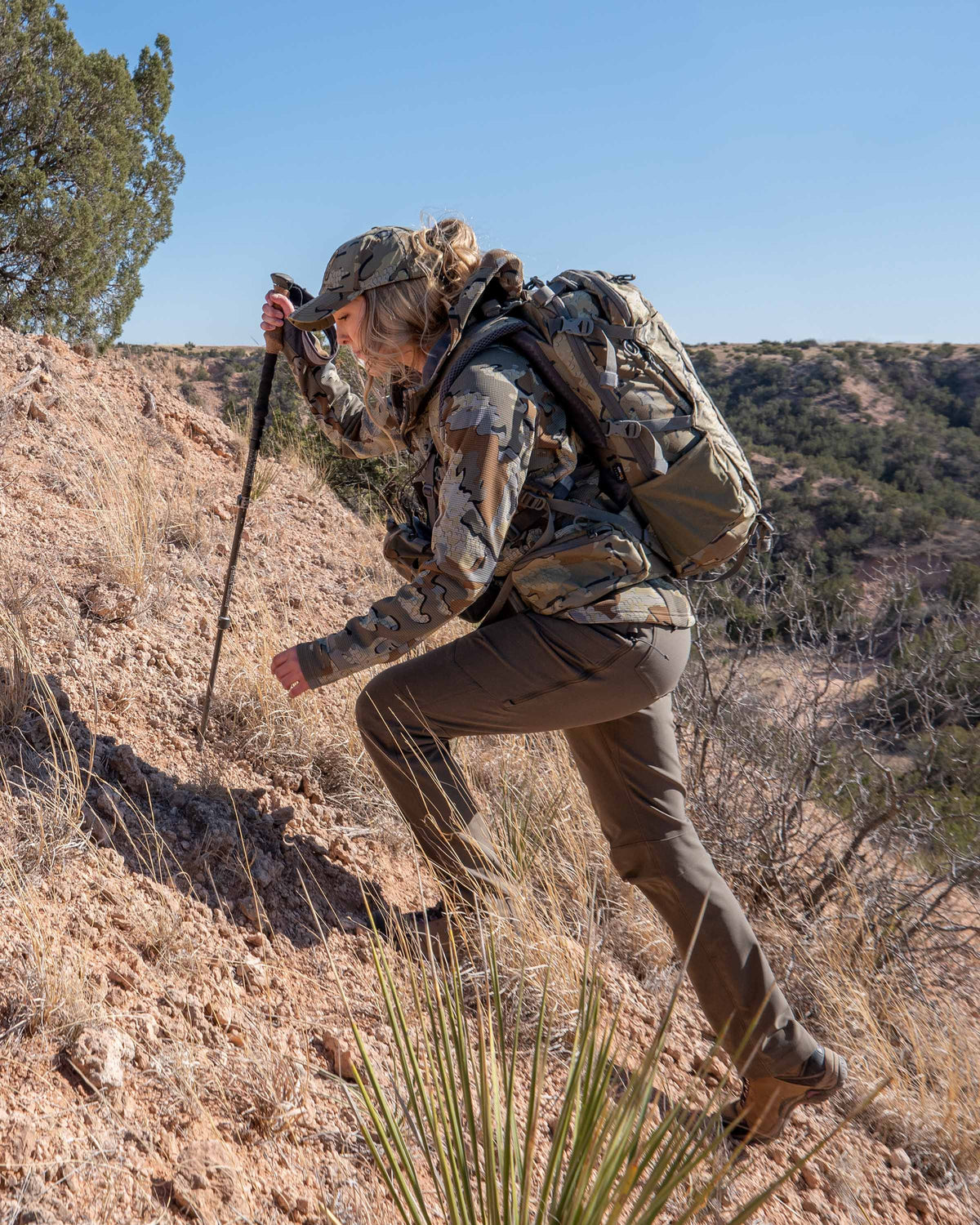 Hunter Hiking Up Open, Brown Hillside Wearing Women's Attack Pants in Ash Brown Color
