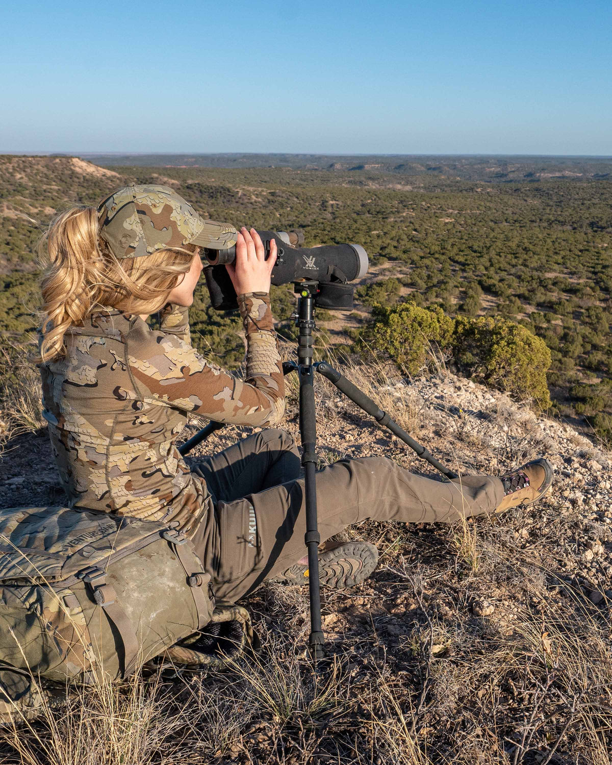 Back, Side Angle of Hunter Glassing Game Through Spotting Scope Wearing Women's Attack Pants in Ash Brown Color