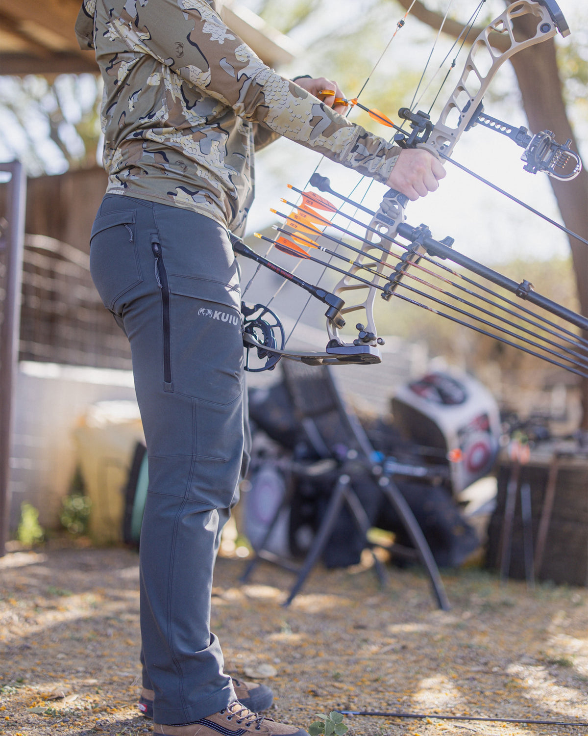 Hunter Holding Bow Wearing Women's Attack Pant in Gunmetal Grey Color Highlighting YKK Zippered Cargo Pockets, Rear Pockets and Hip Vents.