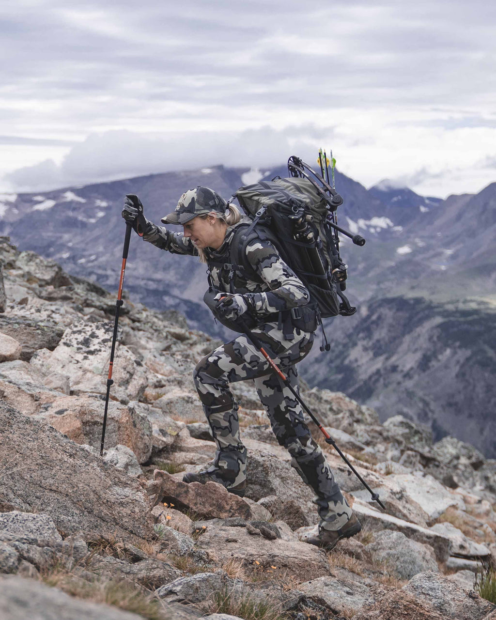 Female hunter actively climbing rocky area with trekking poles wearing Women's Attack Pant in Vias Camouflage