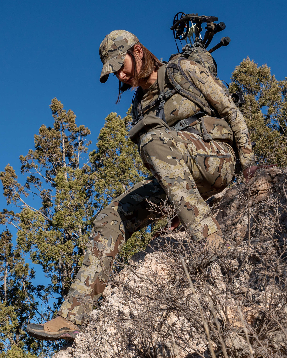 Angled Front View of Hunter Climbing Down Boulder Wearing Women's Attack Pants in Valo Camouflage