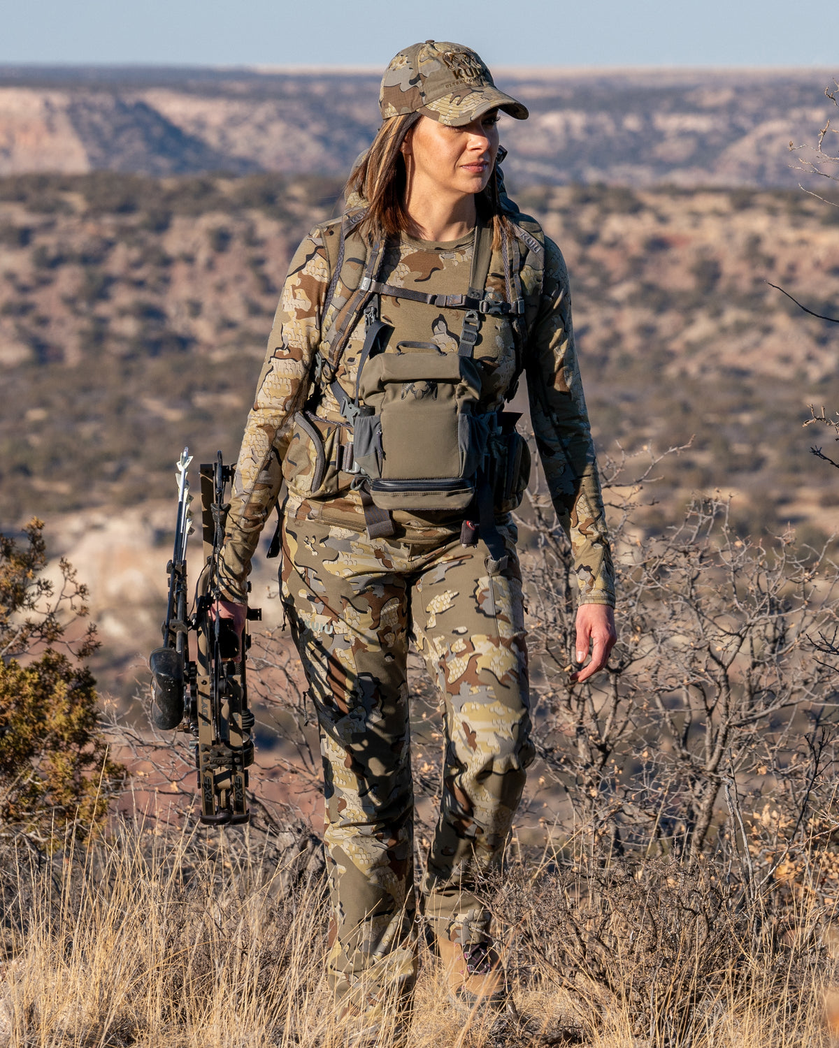 Female hunter walking through field carrying bow wearing Women's Attack Pant in Valo Camouflage