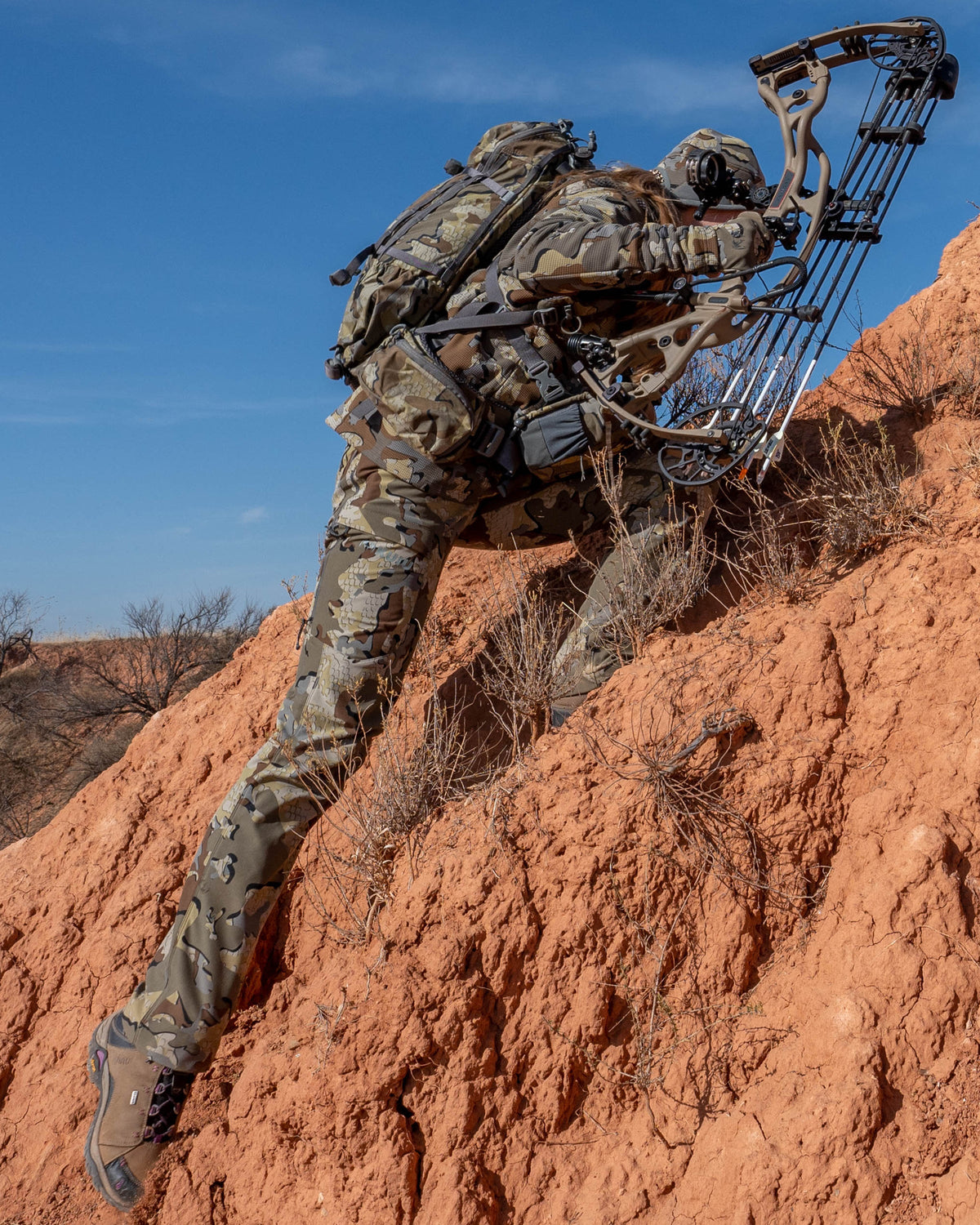 Female hunter climbing steep terrain holding bow wearing Women's Attack Pant in Valo Camouflage