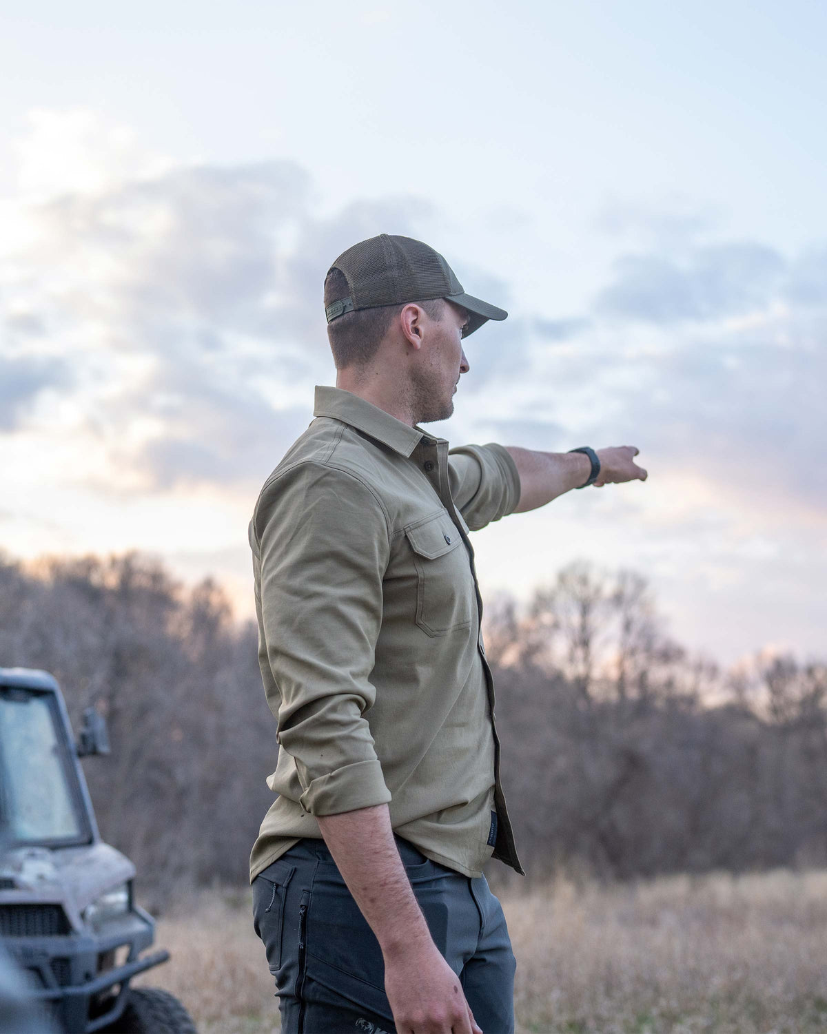 Side view of Hunter wearing Motive LS Work Shirt in Khaki, pointing into the distance