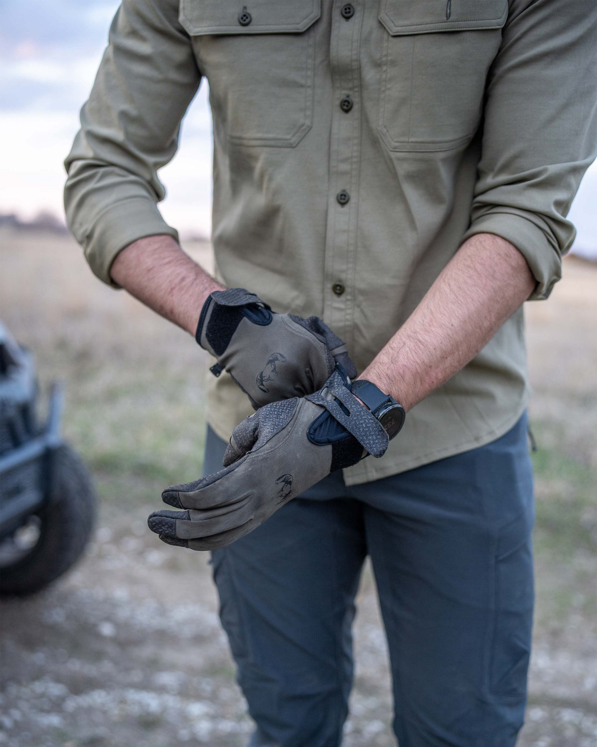 Close-up of Hunter adjusting his gloves, wearing Motive LS Work Shirt in Khaki