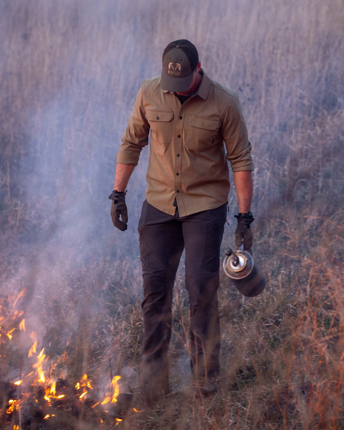 Hunter stands next to a controlled line of flame, carrying a drip torch, wearing Motive LS Work Shirt in Khaki