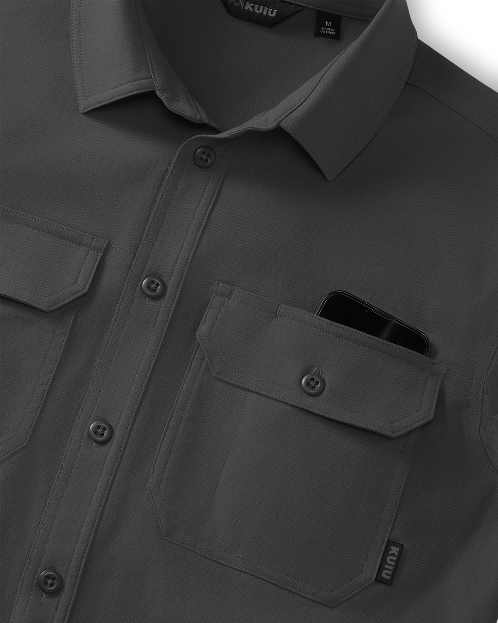 Close-up of Motive Short Sleeve Workgrade Button‑up Shirt in Asphalt Grey showing the collar, button placket, and dual chest pockets, with a smartphone partially visible inside one pocket.