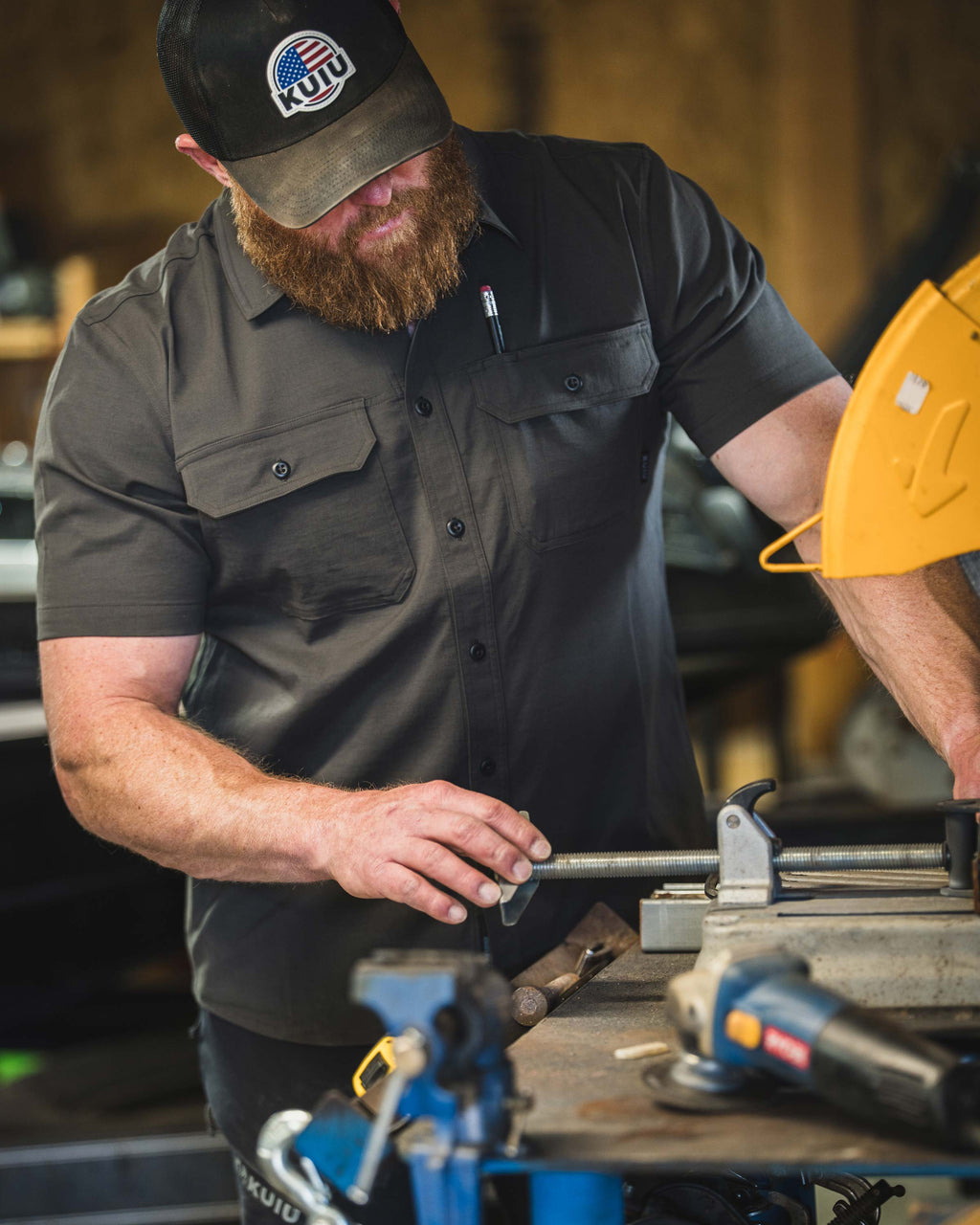 Man wearing Motive Short Sleeve Workgrade Shirt in Asphalt Grey using a metal cutting machine on a workbench inside a workshop.