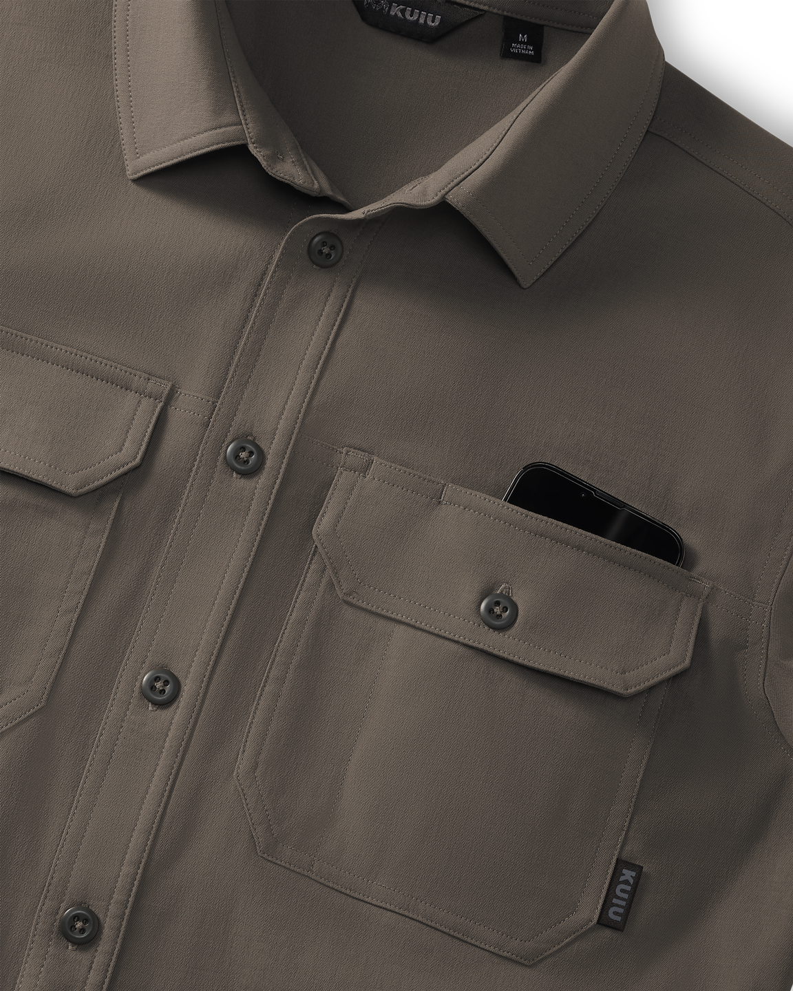 Close-up of Motive Short Sleeve Workgrade Button‑up Shirt in Rodeo Brown showing the collar, button placket, and dual chest pockets, with a smartphone partially visible inside one pocket.