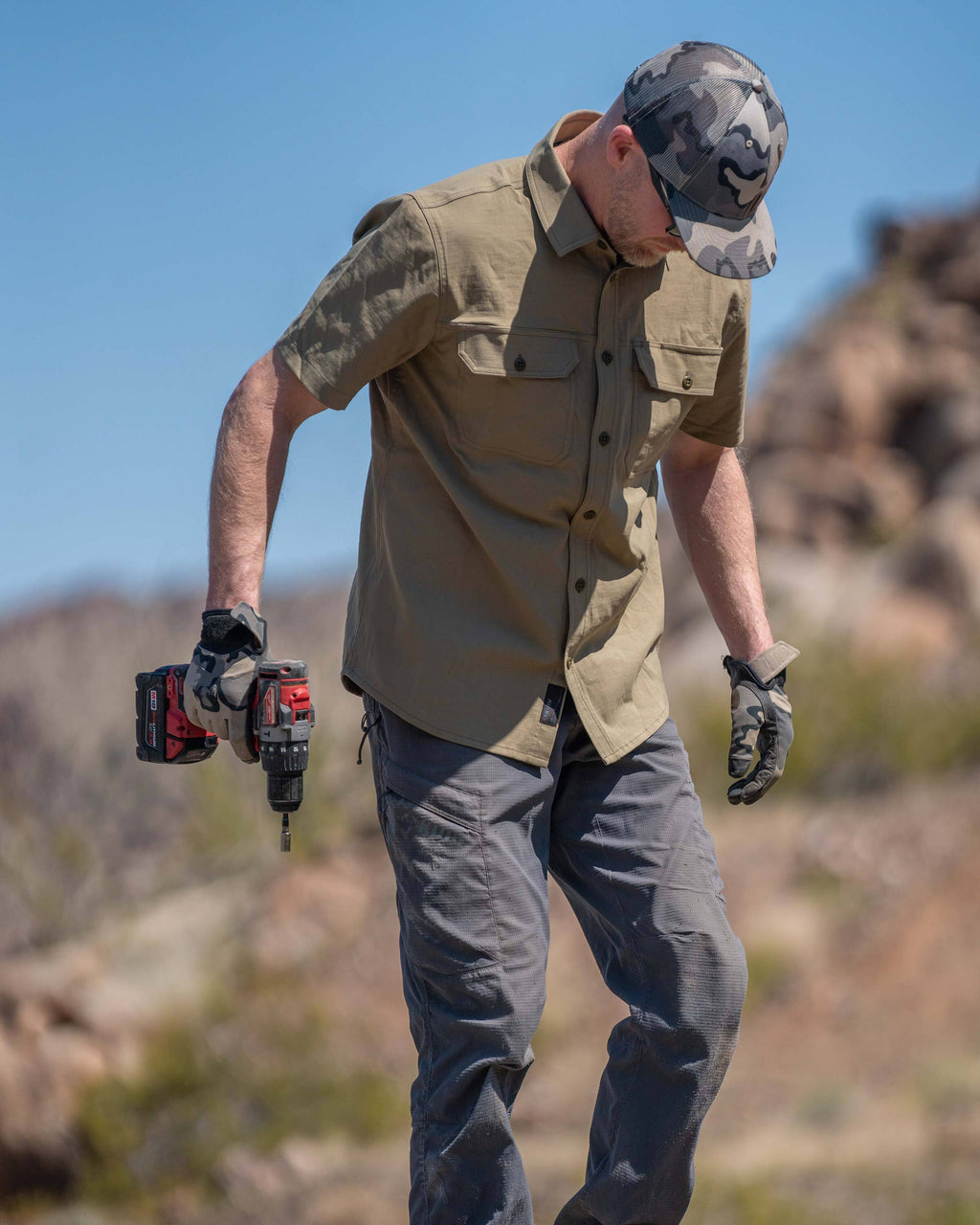 Model looking down, holding a cordless screwdriver, wearing Motive Short Sleeve Work Shirt in Khaki