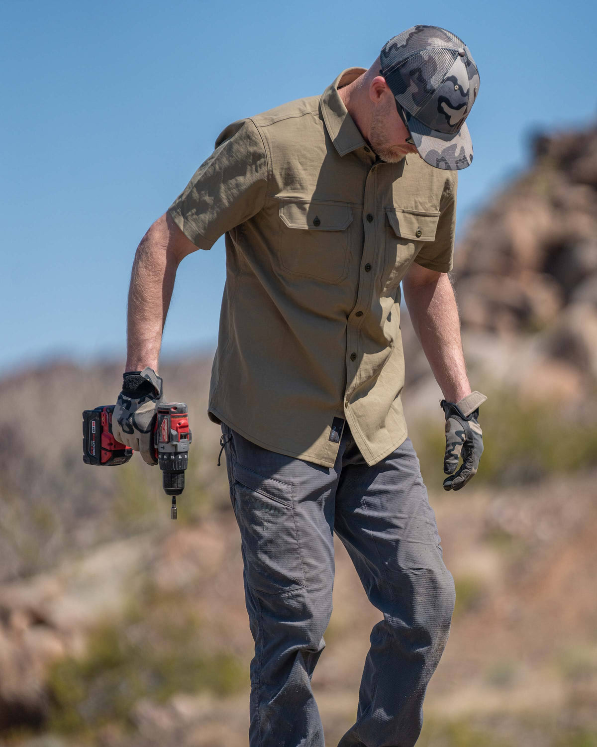 Model looking down, holding a cordless screwdriver, wearing Motive Short Sleeve Work Shirt in Khaki