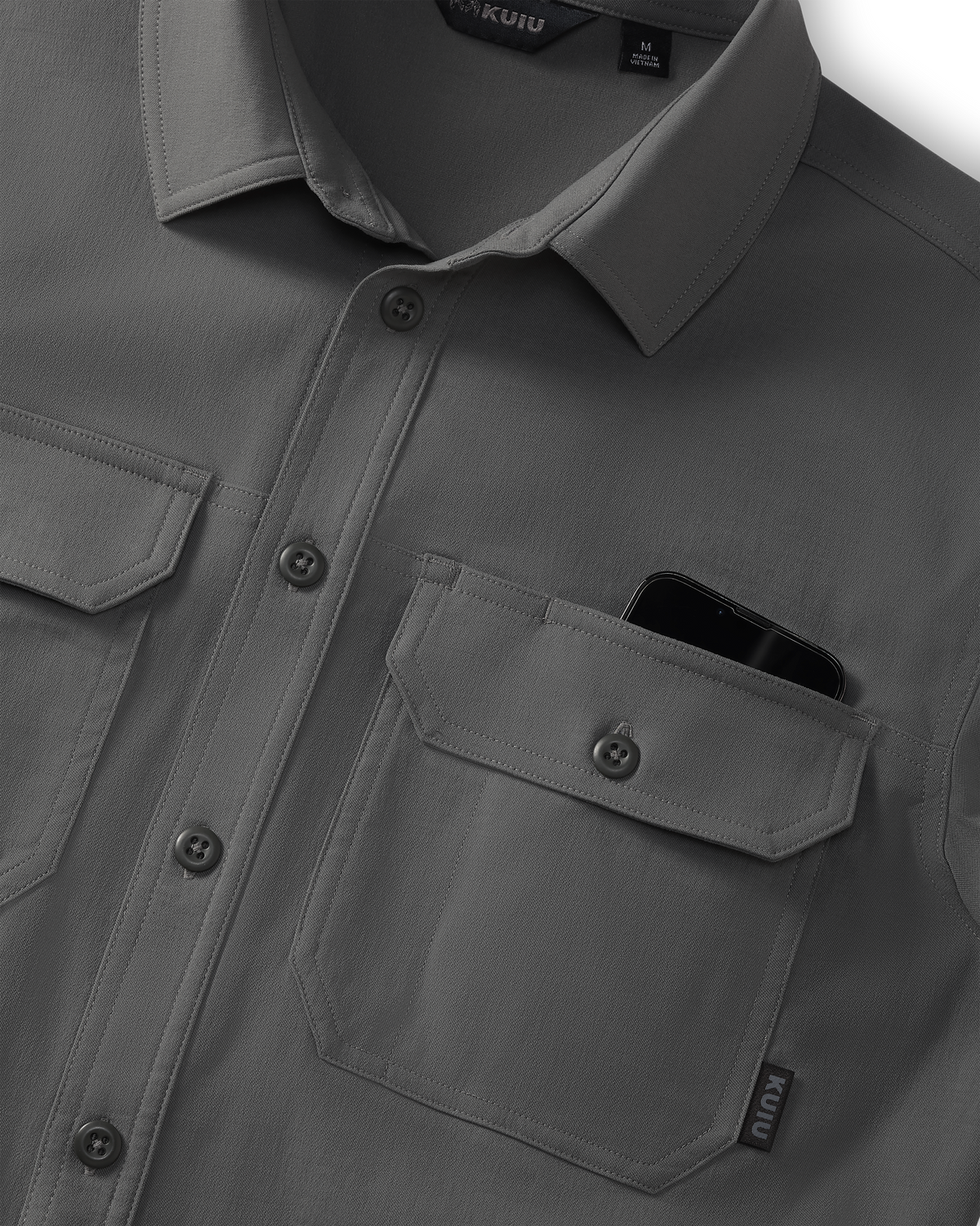 Close-up of Motive Short Sleeve Workgrade Button‑up Shirt in Stone Grey showing the collar, button placket, and dual chest pockets, with a smartphone partially visible inside one pocket.