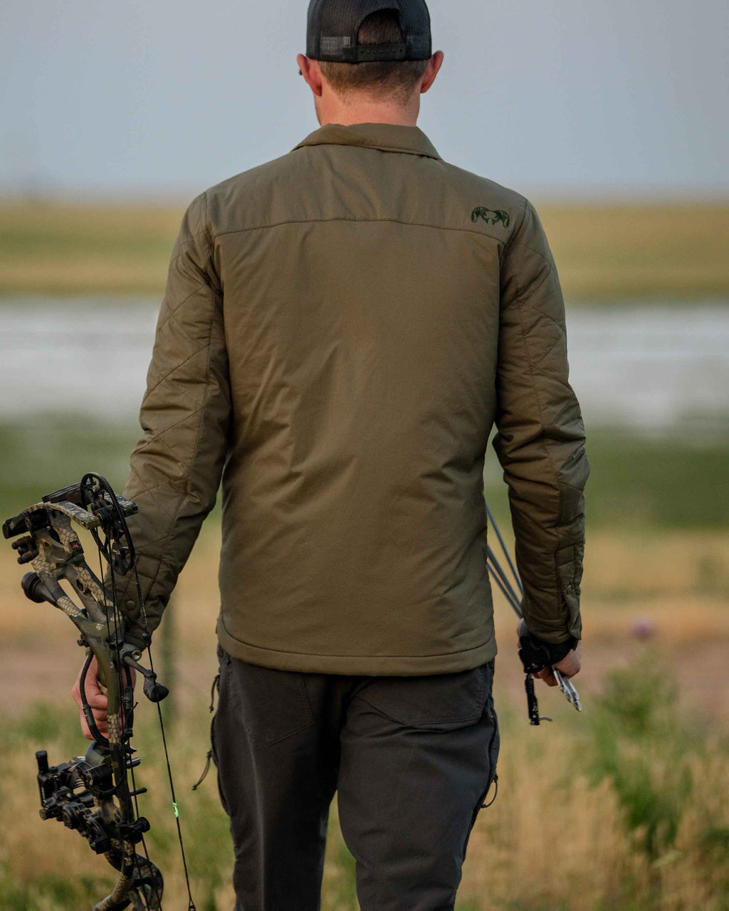 Back of Base Camp Insulated Snap Shirt in Ash Brown with hunter holding bow in an open field