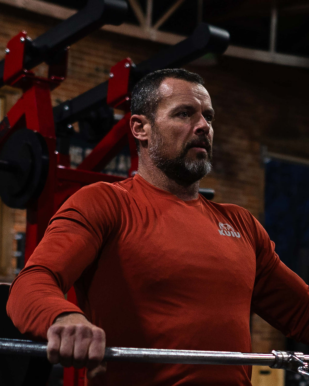 Man using a rowing machine, wearing Velocity LS Crew in Rust Red