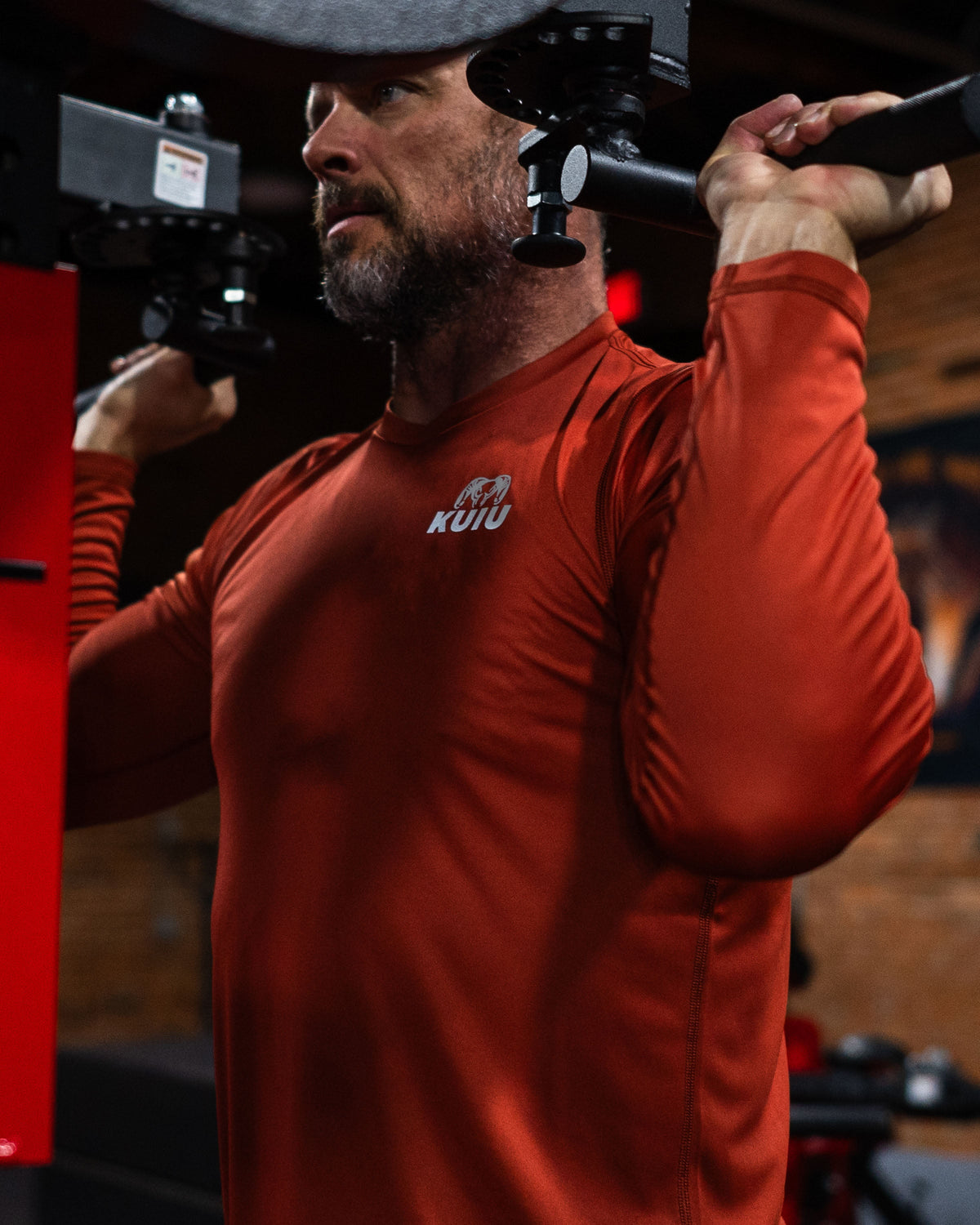 Man in a workout position performing shoulder press, wearing Velocity LS Crew in Rust Red
