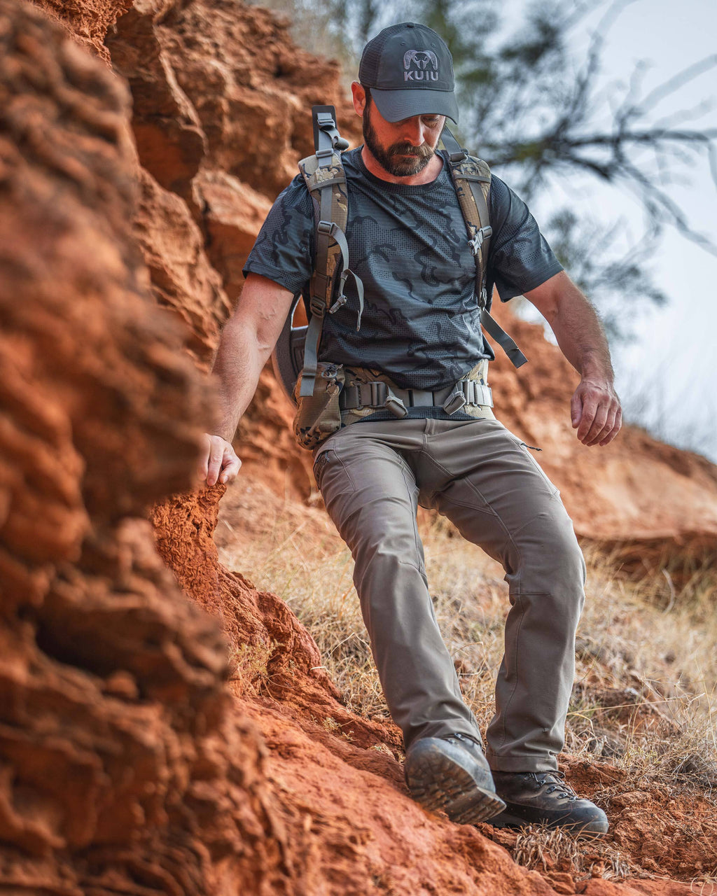 A man hiking down a steep red rock slope wearing a TrailTrainer Short Sleeve Crew in Dark Iron Tonal.