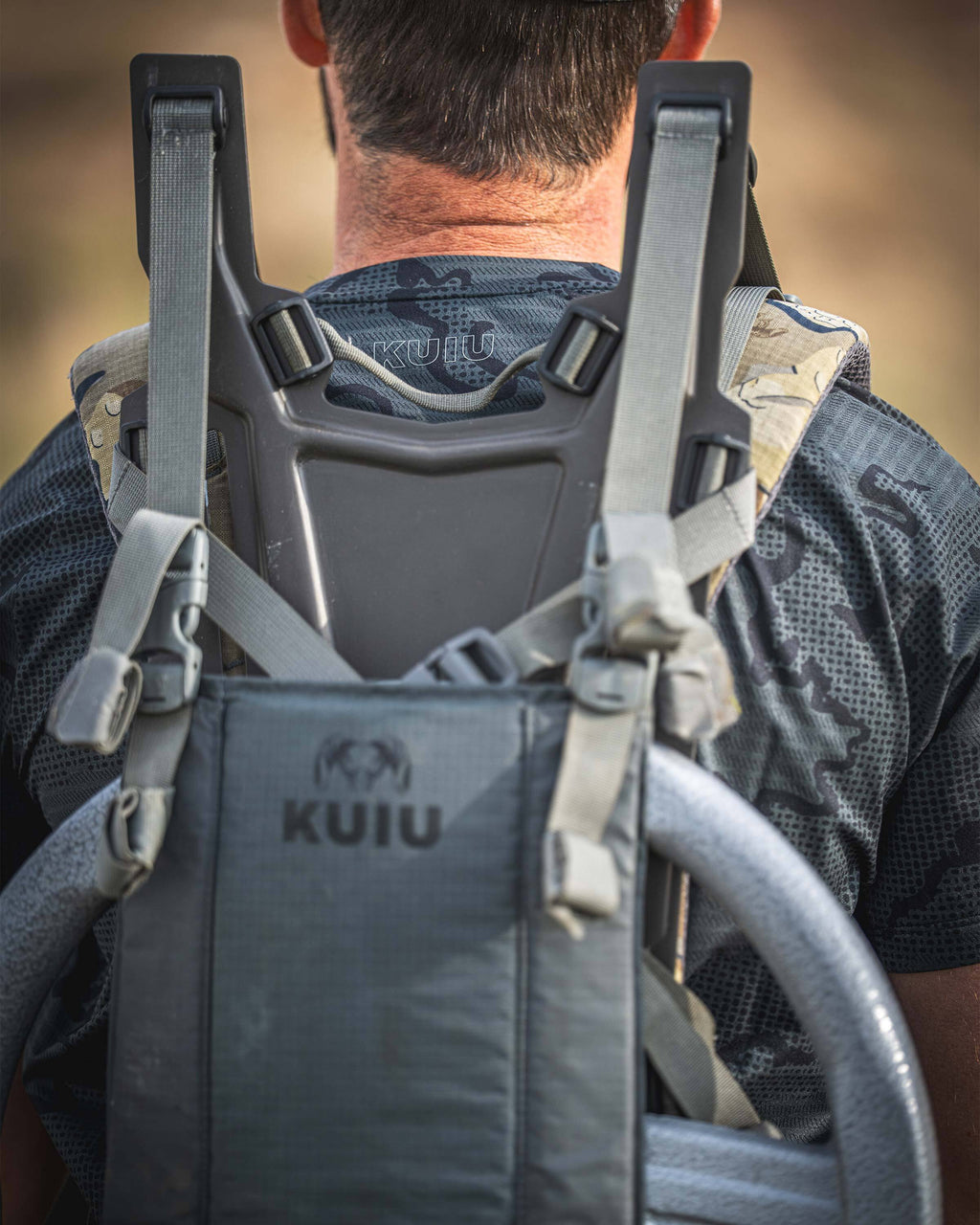 Close-up rear view of a person wearing a TrailTrainer Short Sleeve Crew in Dark Iron Tonal with a suspension and frame strapped with a weight plate.