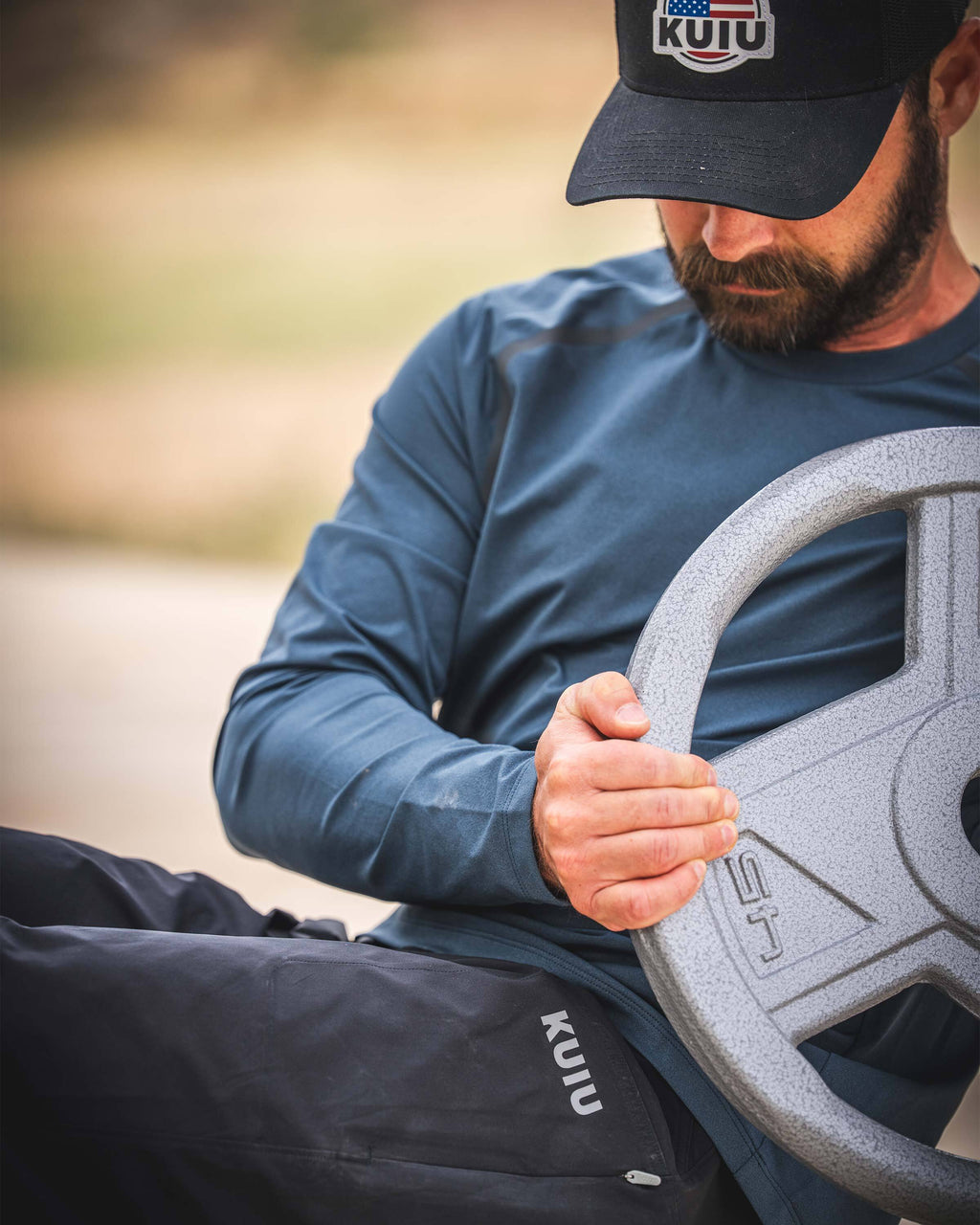 Man wearing TrailTrainer Long Sleeve in Flint Blue working out with a weight plate.