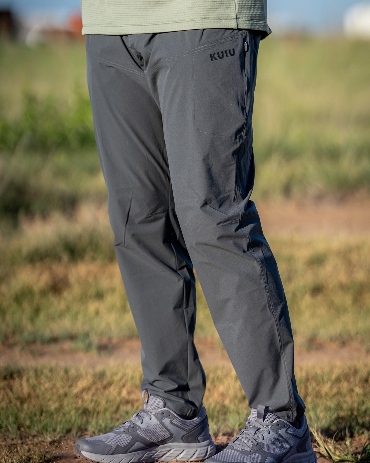 Close-up of a person wearing TrailTrainer Pant in Cast Iron in an outdoor setting, standing outdoors on a green lawn.