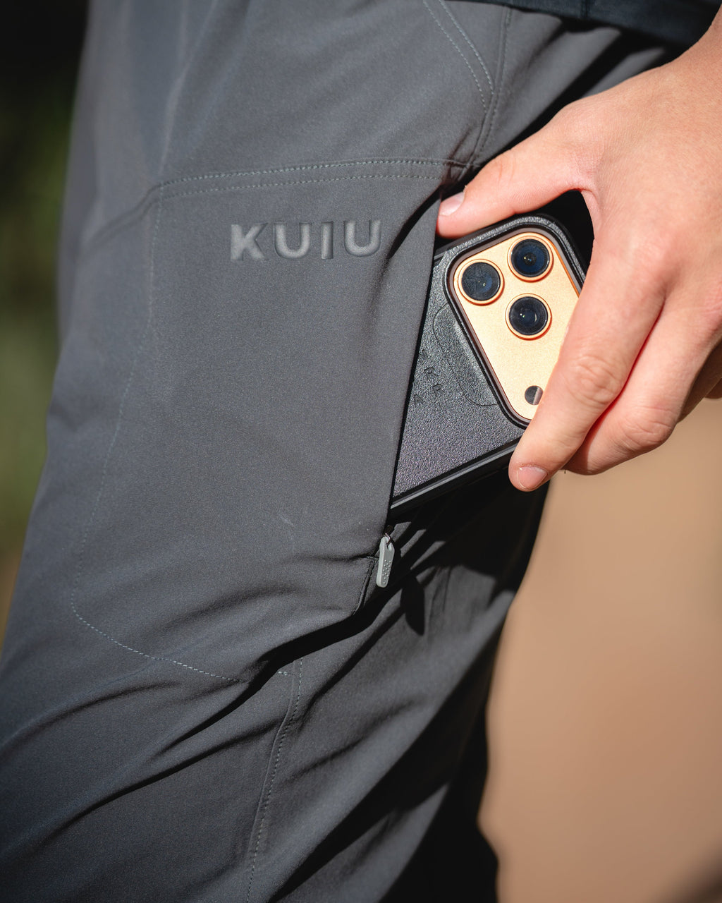 Close-up of a person wearing TrailTrainer pant in Cast Iron Grey, showing a side pocket with a phone tucked into the pocket. 