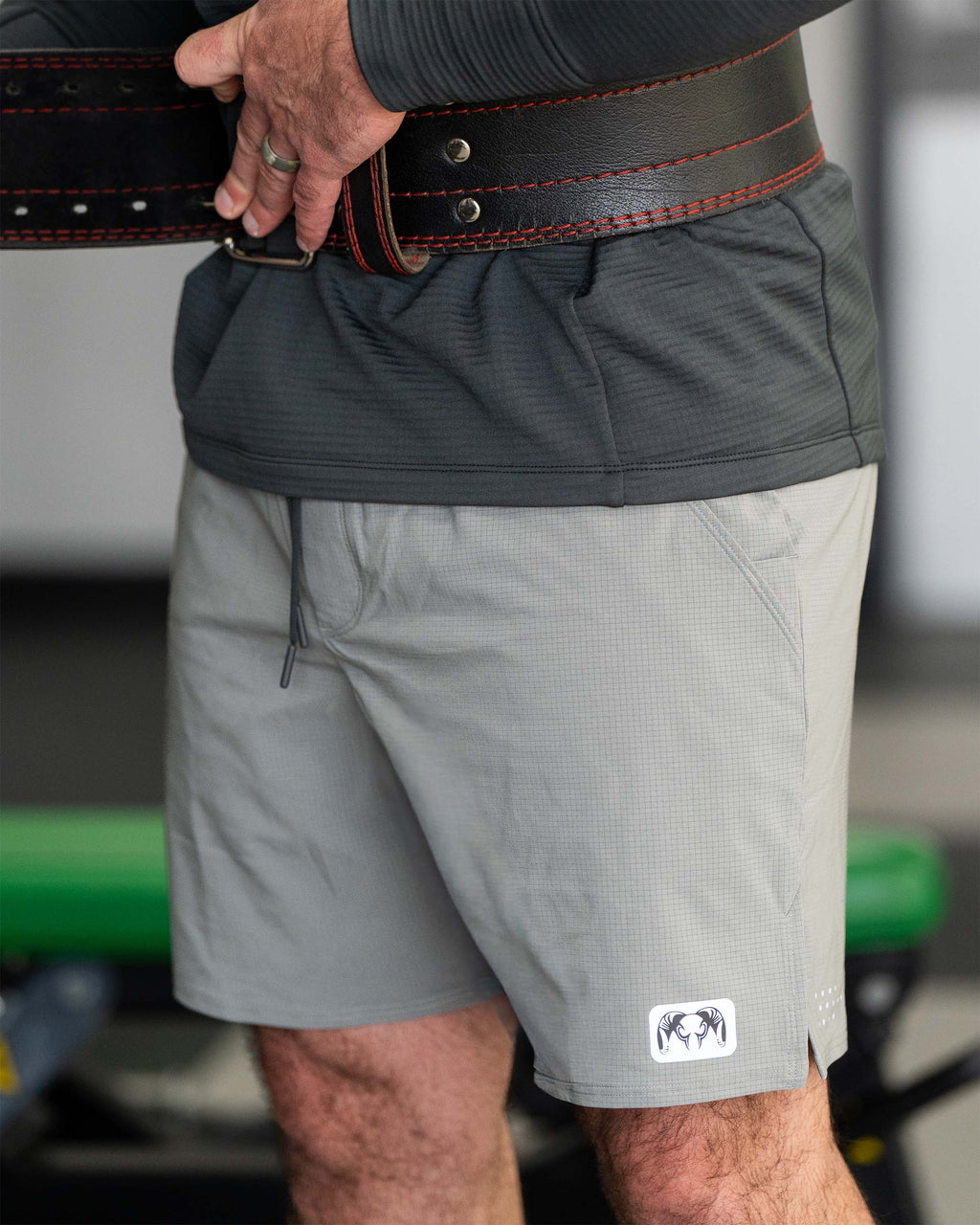 Close-up of a man adjusting a black weightlifting belt around the waist wearing  EnduroTrainer 7" Short in Shadow Grey