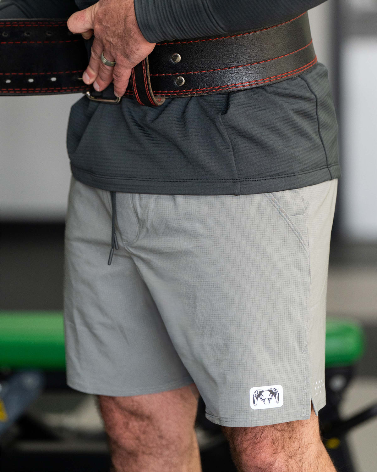 Close-up of a man adjusting a black weightlifting belt around the waist wearing  EnduroTrainer 7" Short in Shadow Grey