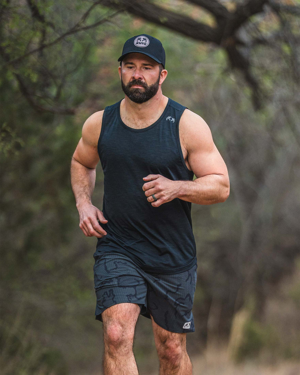 Man in an outdoor setting, running on a trail, wearing an EnduroMesh Tank in Black.