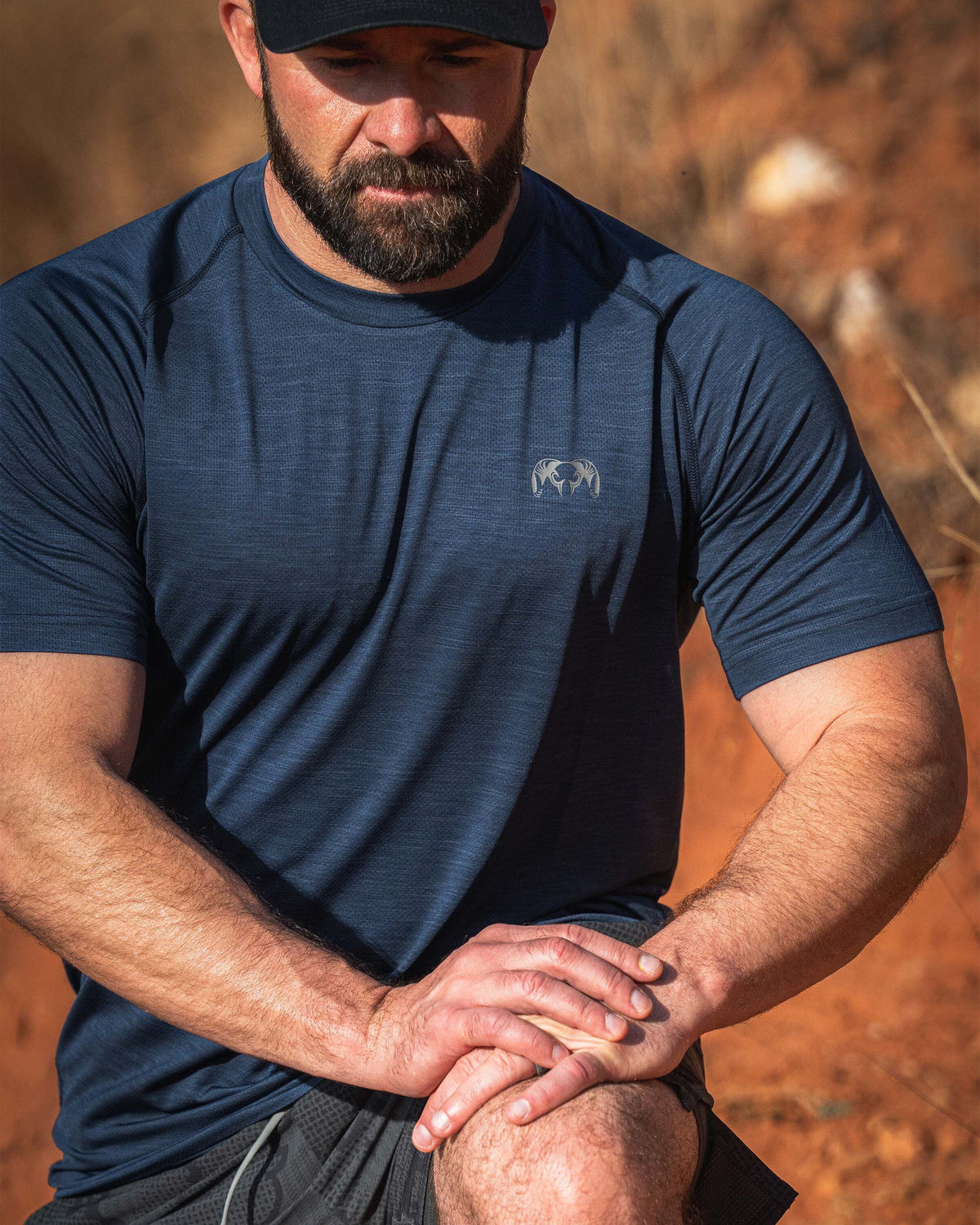 Man wearing an EnduroMesh Short Sleeve Crew in Midnight Blue Heather stretching his legs outdoors on a rocky surface.