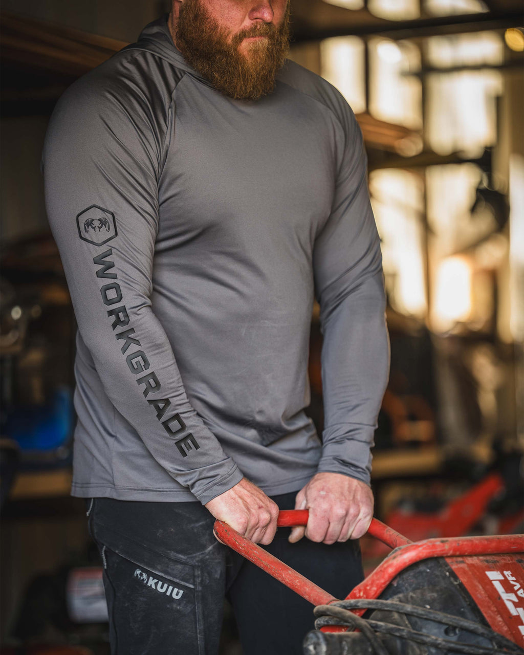 Man in a workshop holding a handle of a generator, wearing Workgrade Long Sleeve Sun Hoodie in Castle Rock Grey.