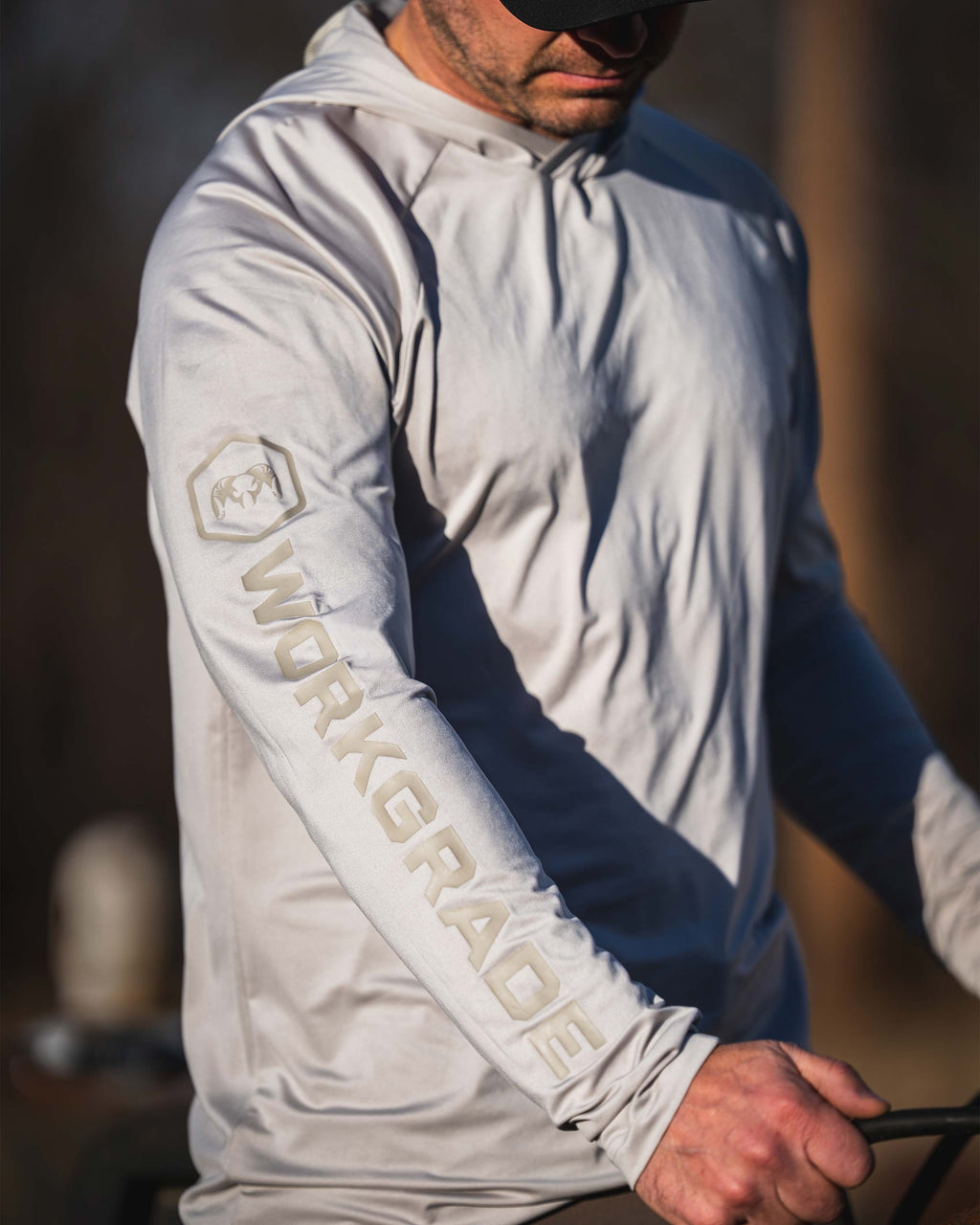 Close-up of a man wearing Workgrade Long Sleeve Sun Hoodie in Haze Grey with “WORKGRADE” printed down the sleeve.