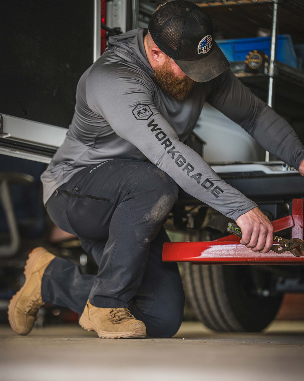 Man kneeling behind a utility vehicle, wearing Workgrade Long Sleeve Sun Hoodie in Castle Rock Grey.